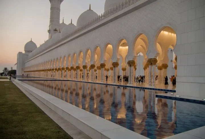 LUMIX G VARIO 14-140/F3.5-5.6 · 15mm · ISO 454 · 1/120s · f/3.6 Arched colonnade of a white grand mosque reflected in a pool at dusk, captured with Caira