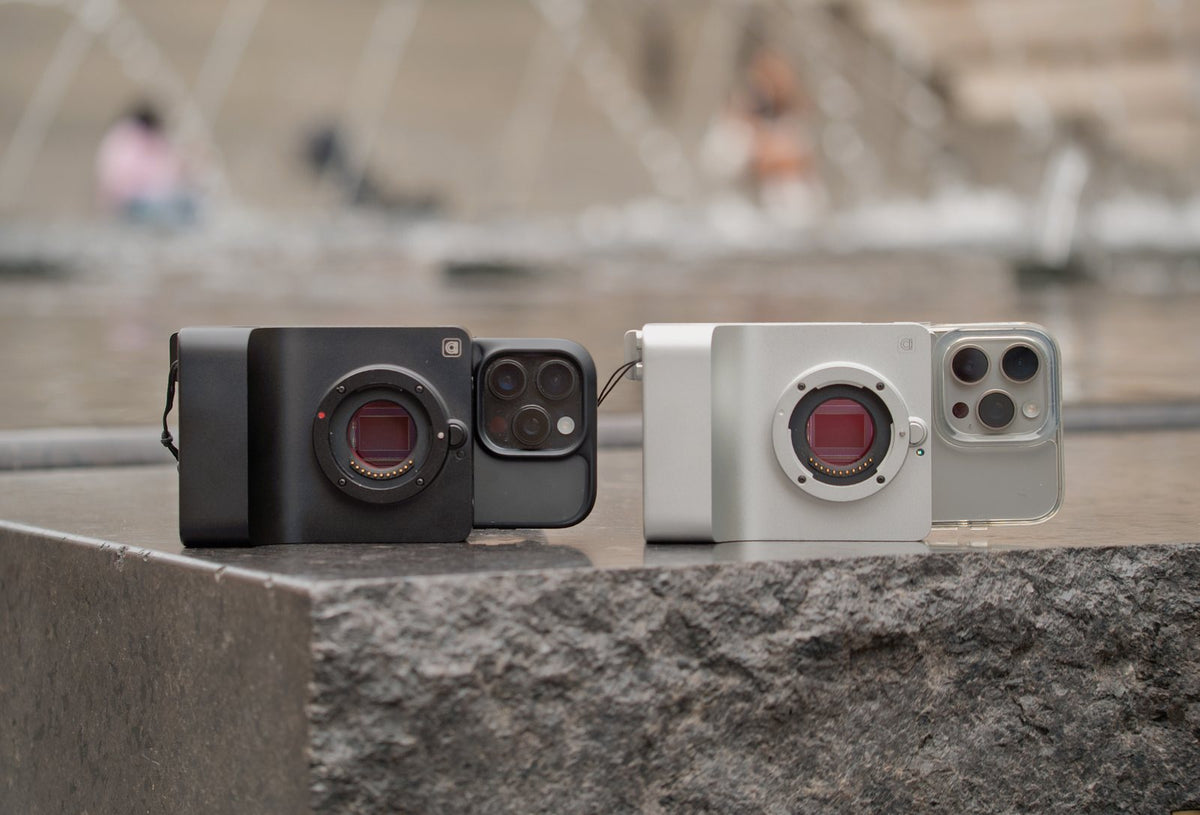 A black Caira and a silver Caira, each with an iPhone attached, side by side on a stone ledge