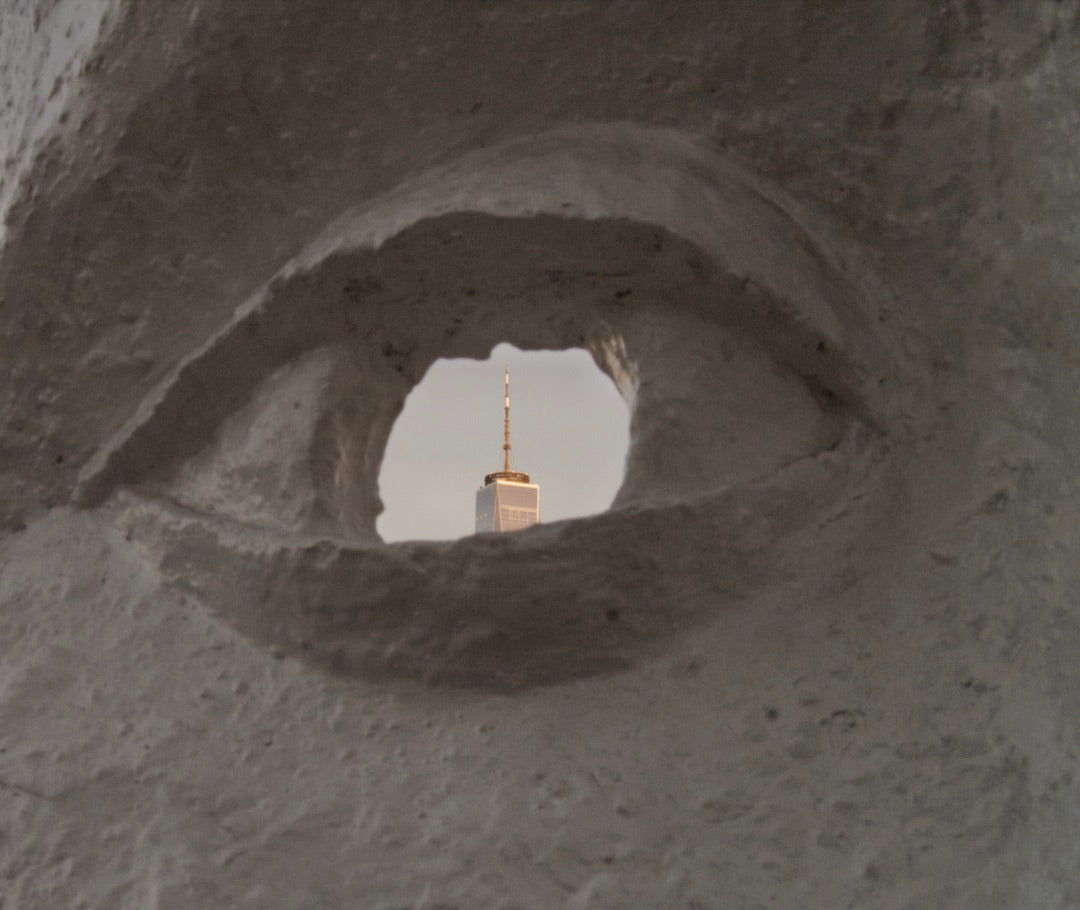 Skyscraper seen through the eye of a carved white sculpture — captured with Caira