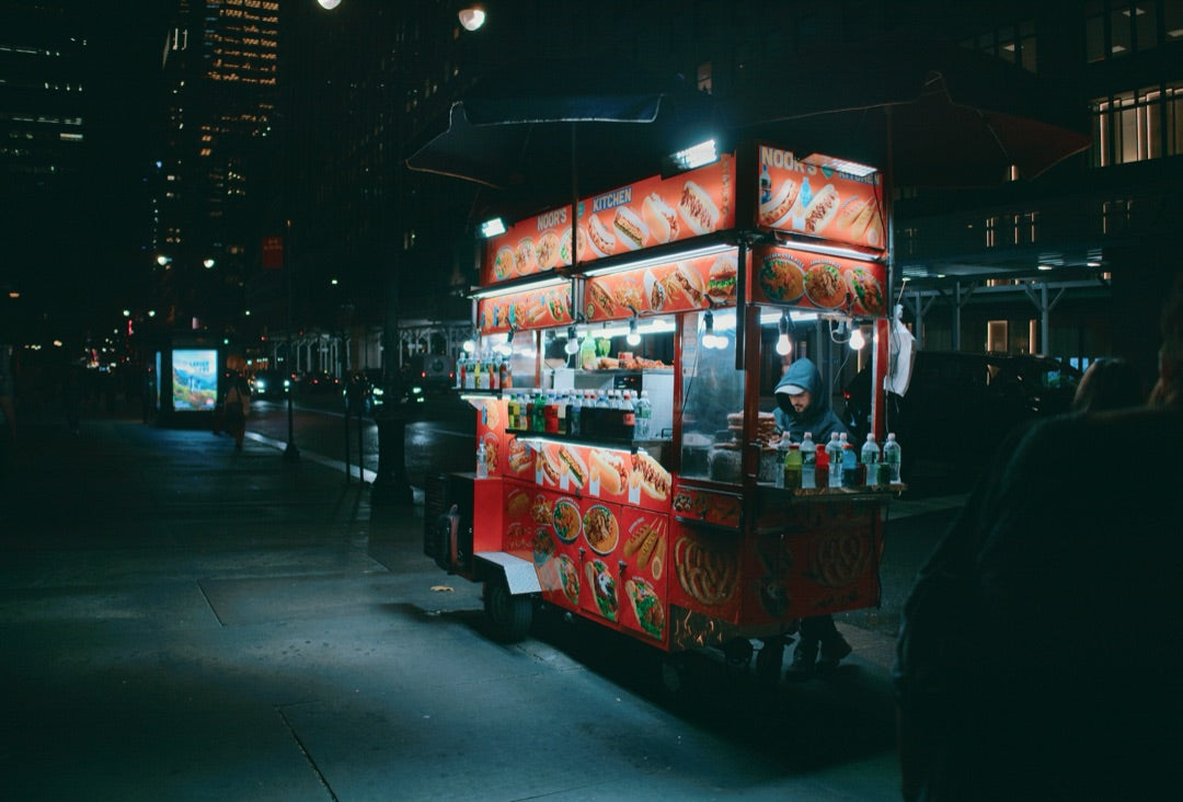 New York hot-dog cart glowing at night on a dark street — captured with Caira