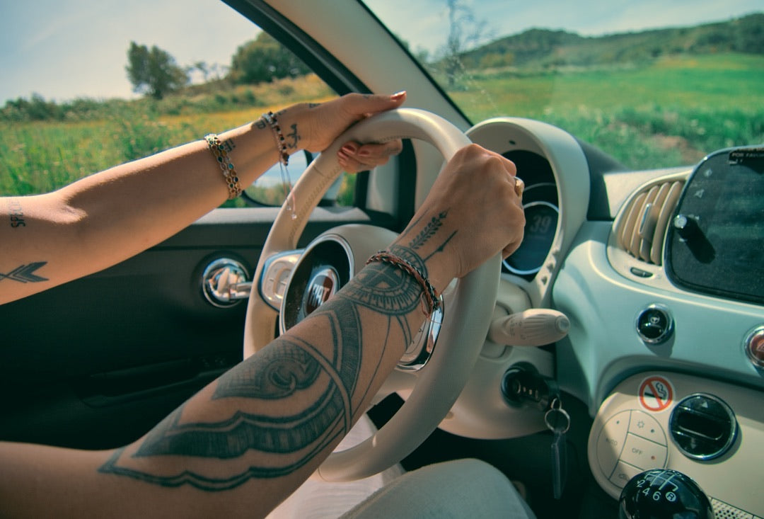 Tattooed hands on a Fiat 500 steering wheel in the countryside