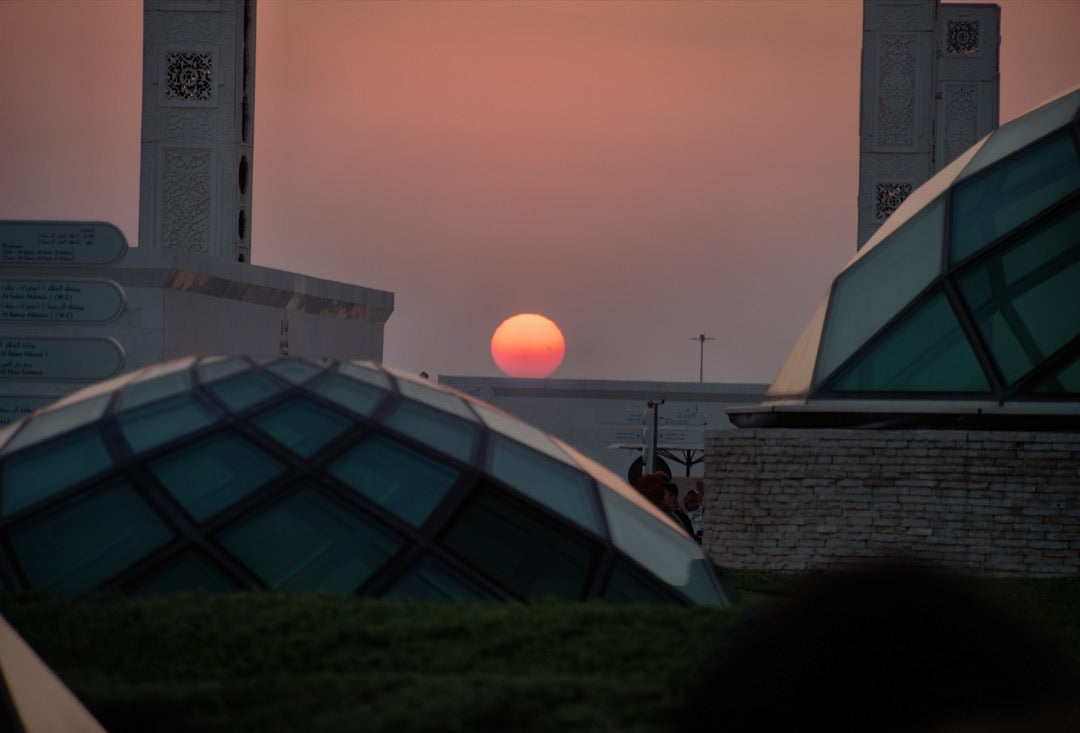 Red sun setting between glass domes and white minaret towers